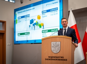 Marszałek Geblewicz przy mównicy prezentuje budżet 2026 roku, w tle slajd z wydatkami i dochodami. 