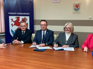 Strony porozumienia podpisują dokument przy stole prezydialnym, obok goście spotkania.