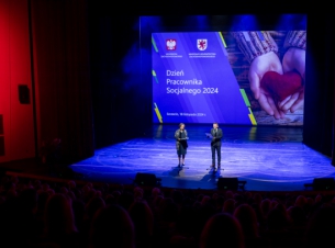 prowadzący galę stoją na scenie, w tle plansza z napisem Dzień Pracownika Socjalnego