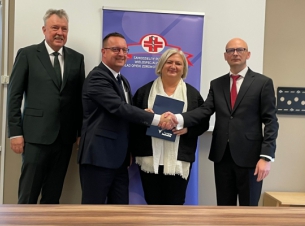 Sygnatariusze porozumienia oraz goście prezentują podpisany dokument, w tle baner szpitala.