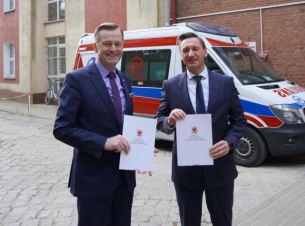 Strony umowy prezentują podpisane porozumienie, w tle budynek ZOL Tuczno oraz ambulans.