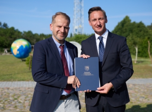 Sygnatariusze umowy prezentują podpisane porozumienie, w tle tereny zielone. 