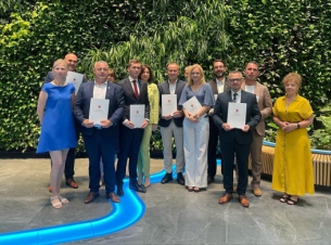 Sygnatariusze umowy prezentują na wspólnej fotografii podpisane porozumienia, w tle zielona ścianka w urzędzie marszałkowskim.