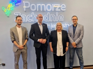 beneficjenci stoją z umowami na tle promocyjnej ścianki z wicemarszałkiem Kowalikiem