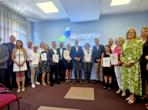 beneficjenci w powiatu koszalińskiego stoją na promocyjnej ściance z marszałekiem i wicemarszałkiem Kowalikiem