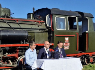 wicemarszałek, prezes KKW i zastępca prezydenta Koszalina wypowiadająsię dla mediów na tle parowozu