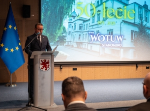 Członek Zarządu Województwa Bogdan Jaroszewicz odczytuje ze sceny list skierowany do uczestników uroczystości, w tle falgi i ekran z logo jubileuszu.