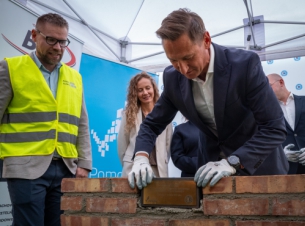 Marszałek Geblewicz wmurowuje kamień węgielny, w tle goście wydarzenia.