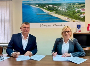 Strony umowy podpisują dokument za stołem prezydialnym.