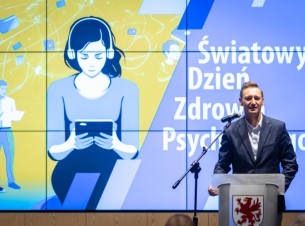 marszałek Olgierd Geblewicz przemawia na scenie, w tle żółto-filoletowy baner z nazwą konferencji 