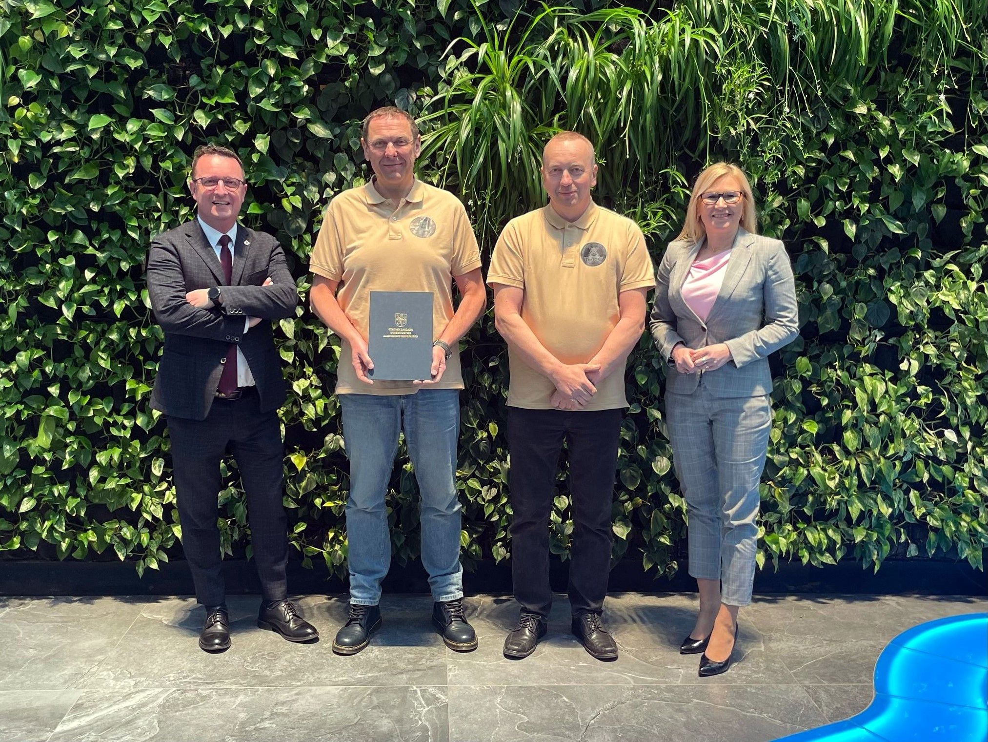 Dotacja dla POSP „Tryton” w Kołobrzegu. Sygnatariusze umowy prezentują podpisane porozumienie na zielonej ściance Urzędu Marszałkowskiego.