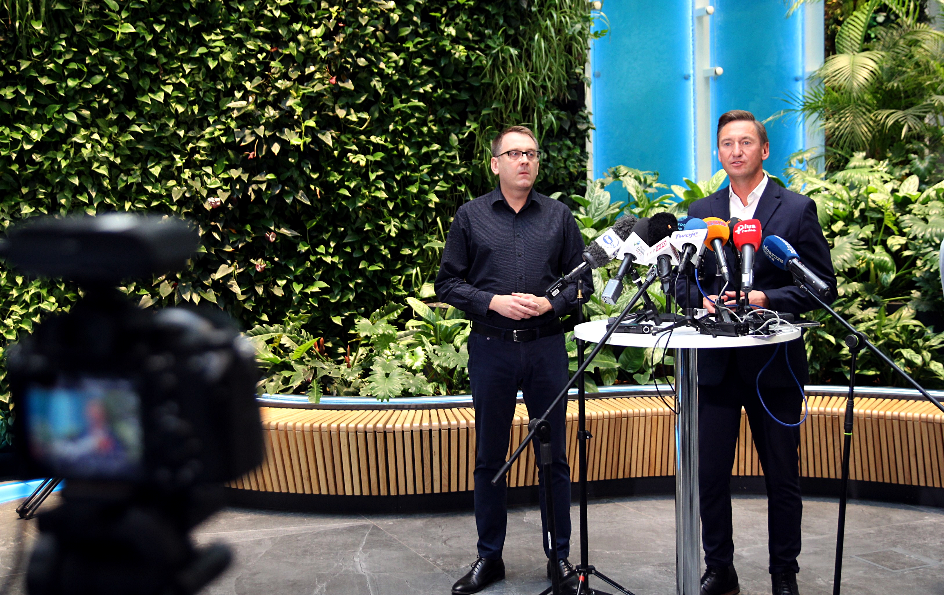 Dawid Krystek, Olgierd Geblewicz i Gabriela Wiatr podczas konferencji prasowej. Stoją na tle roslinnej ściany i niebieskiego panelu z wodą