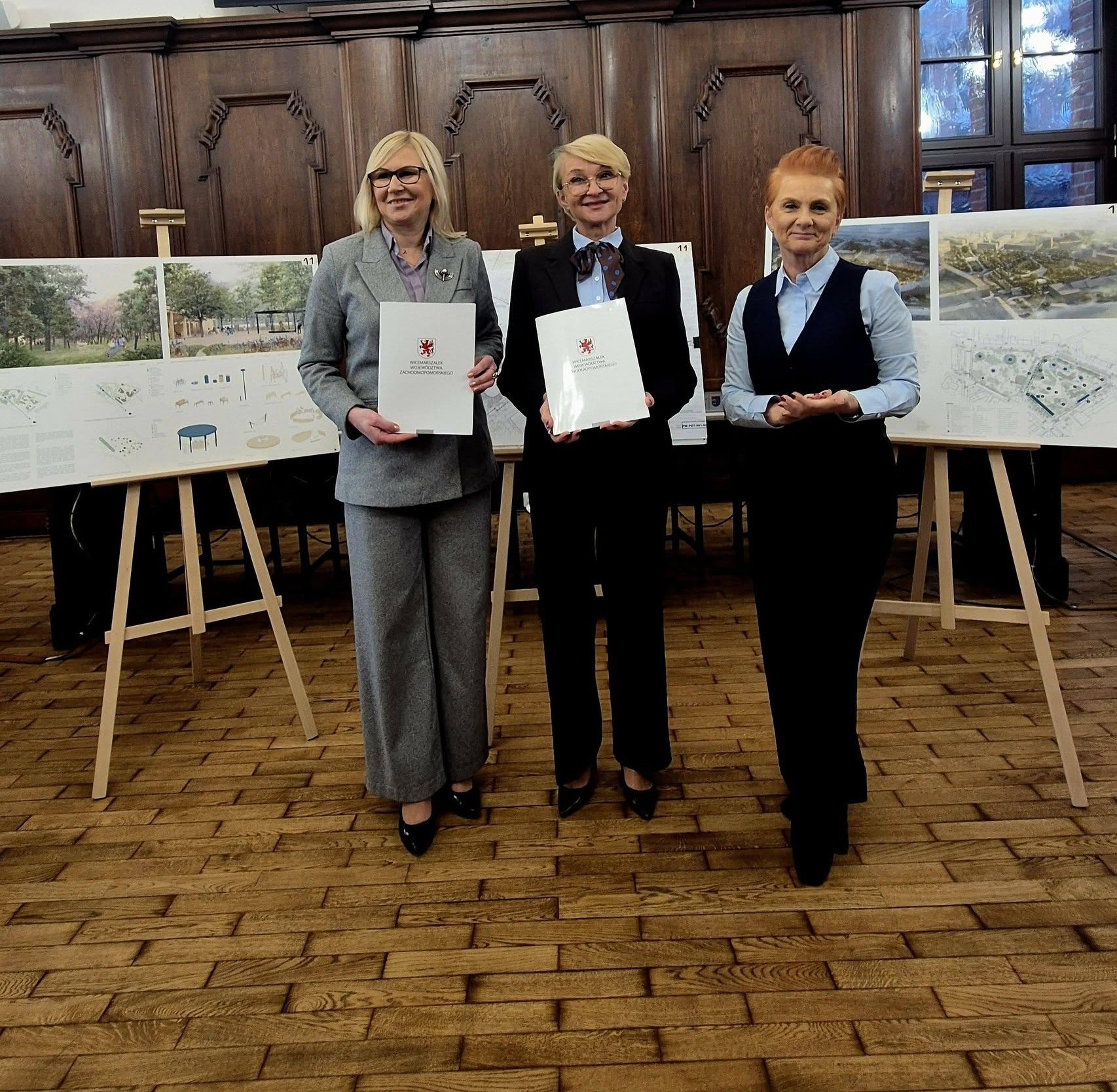 Unijna dotacja dla Kołobrzegu na rewitalizację Skweru Pionierów. Strony porozumienia prezentują podpisany dokument, w tle wystrój ratusza i wizualizacje miejsca po zmianach.